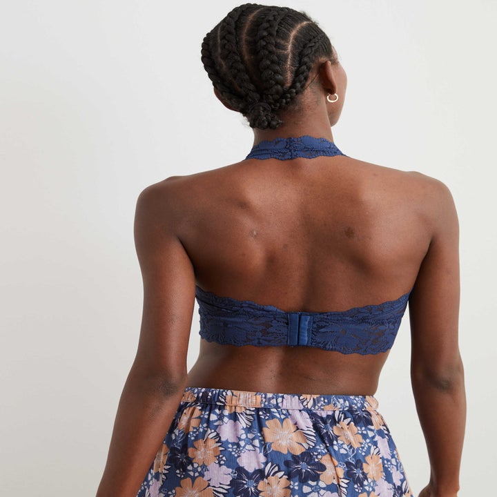 the model showing the back of the bralette with a hook and eye closure in the center of the back and a halter strap around the neck
