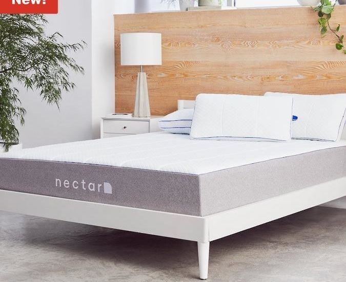 A Nectar brand mattress with a gray fabric on the sides and a plush white top on a white bed frame