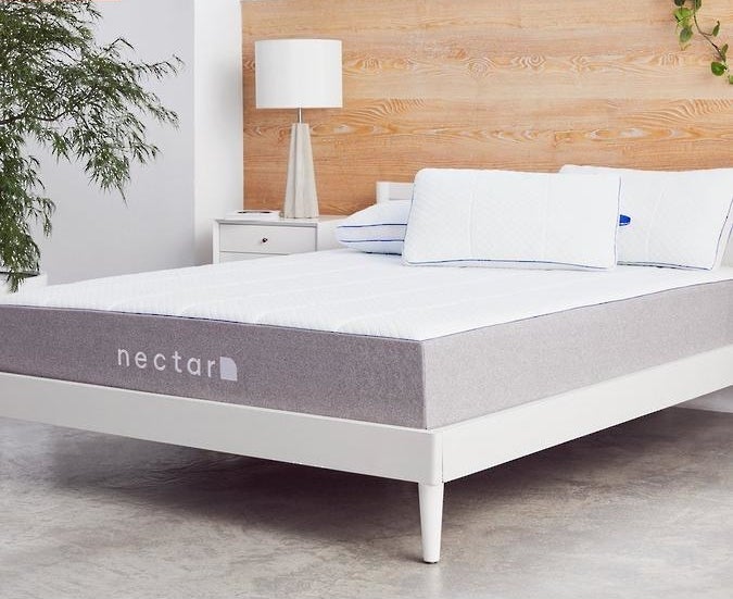 A Nectar brand mattress with a gray fabric on the sides and a plush white top on a white bed frame