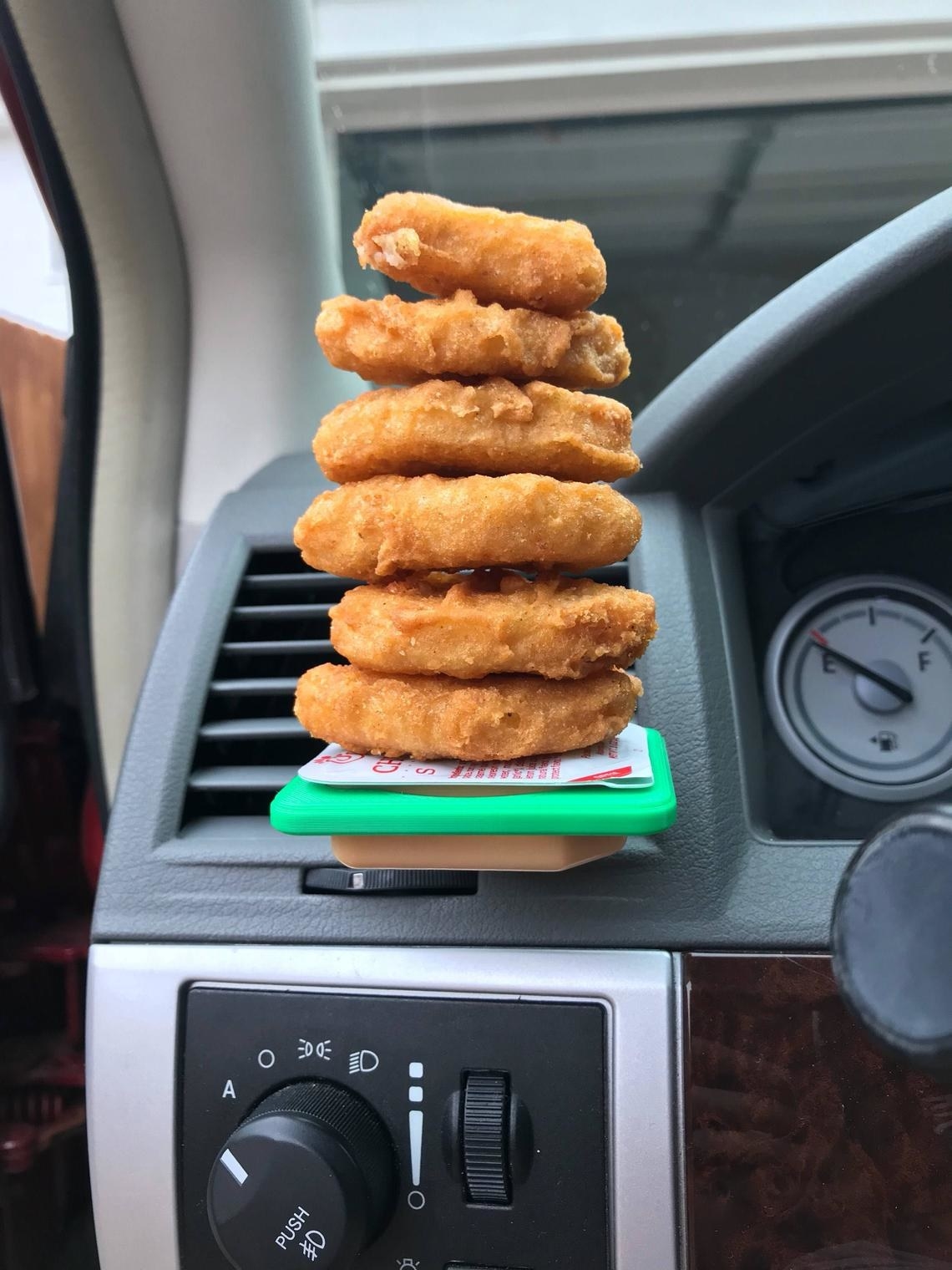 inside car with a fast food dipping sauce holder clipped onto a vent. Sauce in the clip with chicken nuggets stacked vertically on it to show strength of product