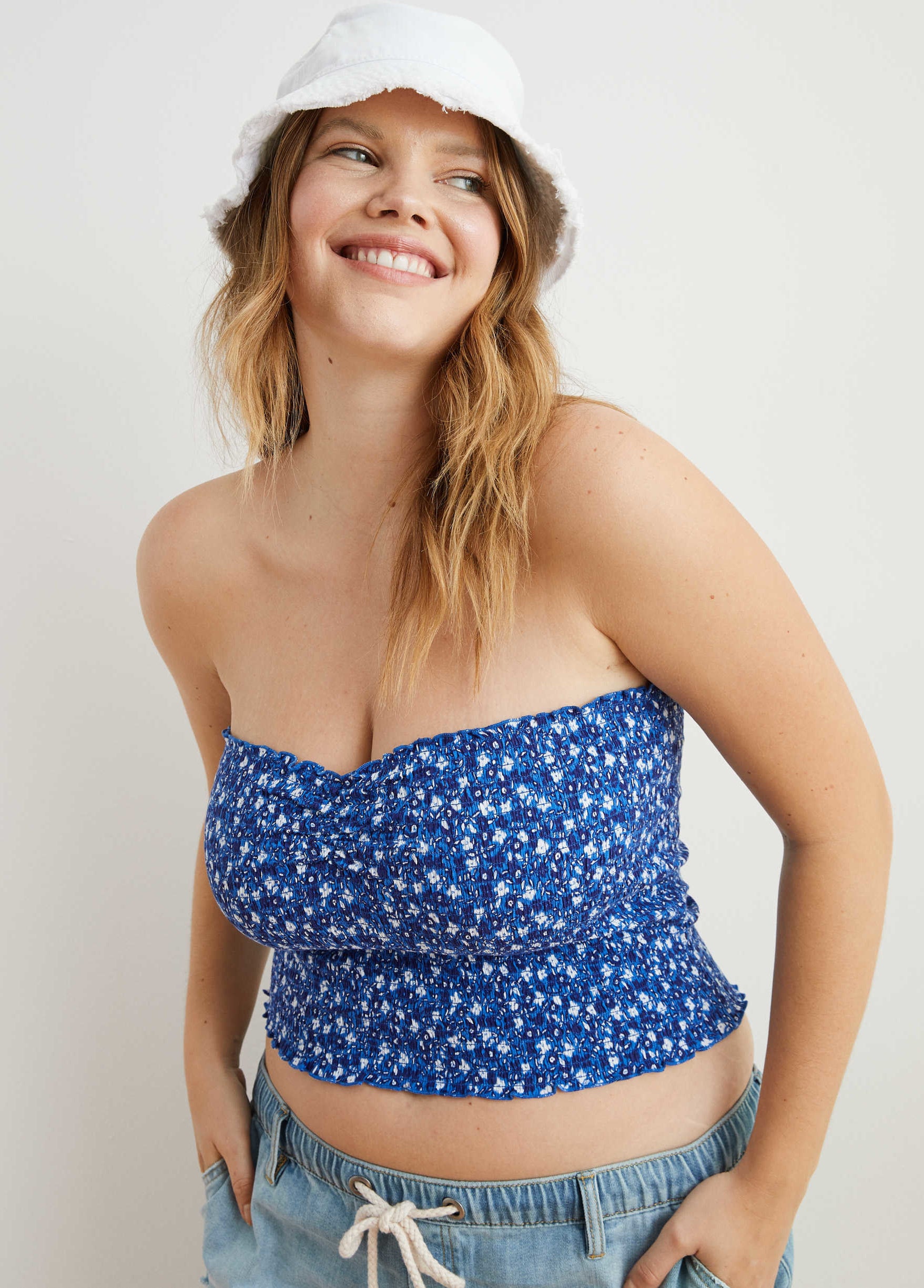 model in a ruched tube top that&#x27;s cropped right below the belly button in a small floral print styled with a bucket hat and tie-waist jean shorts