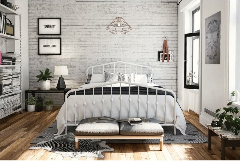 A bedroom with a bed propped on a white-painted platform bed frame with spokes with round finials in the middle of them 