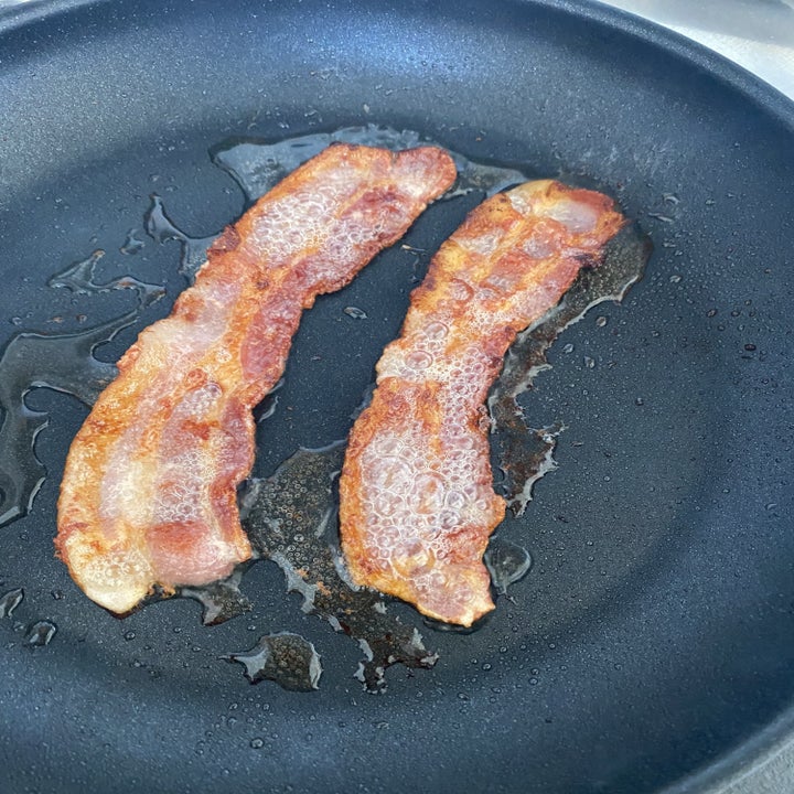 Two slices of bacon frying in a skillet.