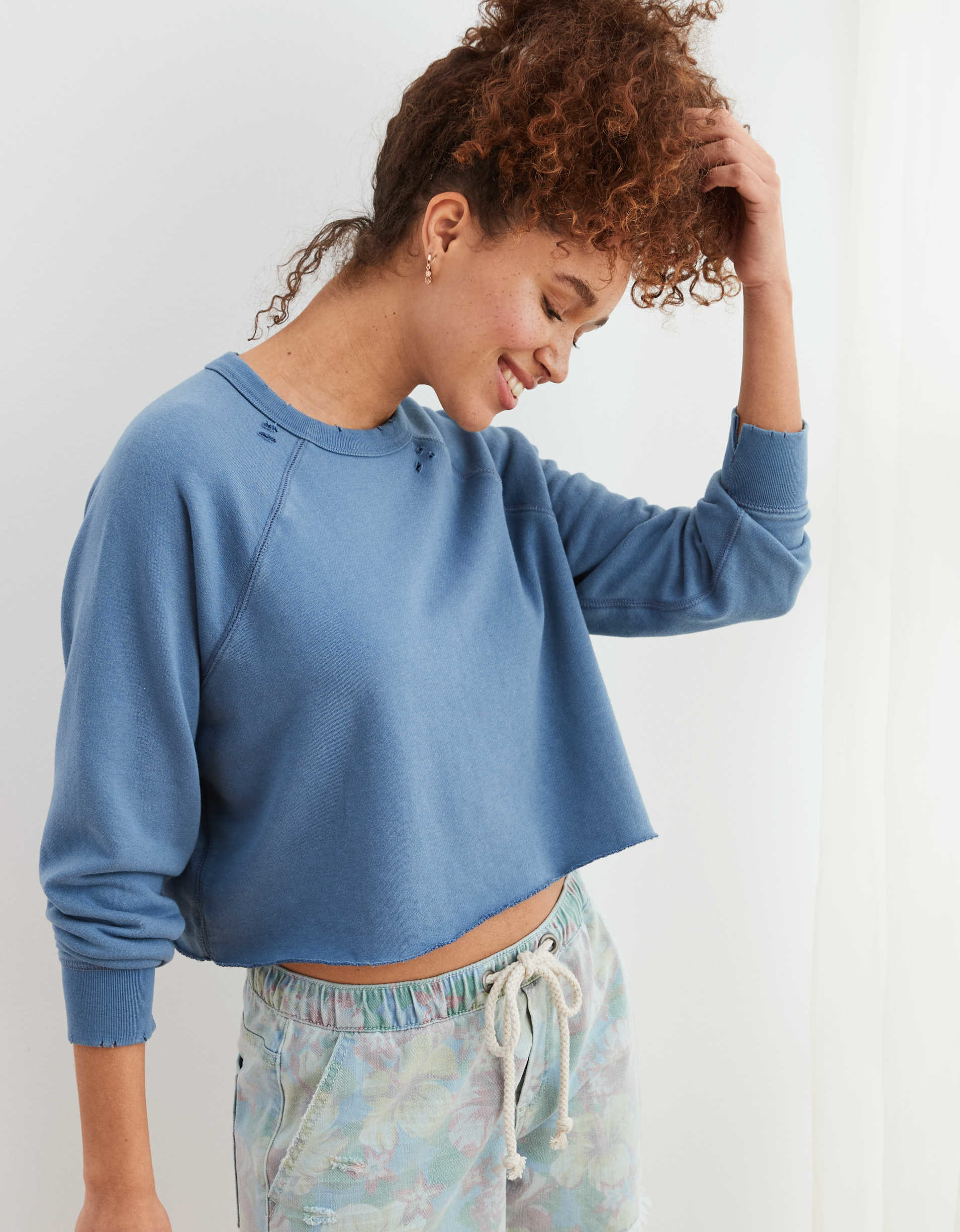 model in a slightly cropped blue crewneck sweatshirt with tiny holes near the beck and wrists