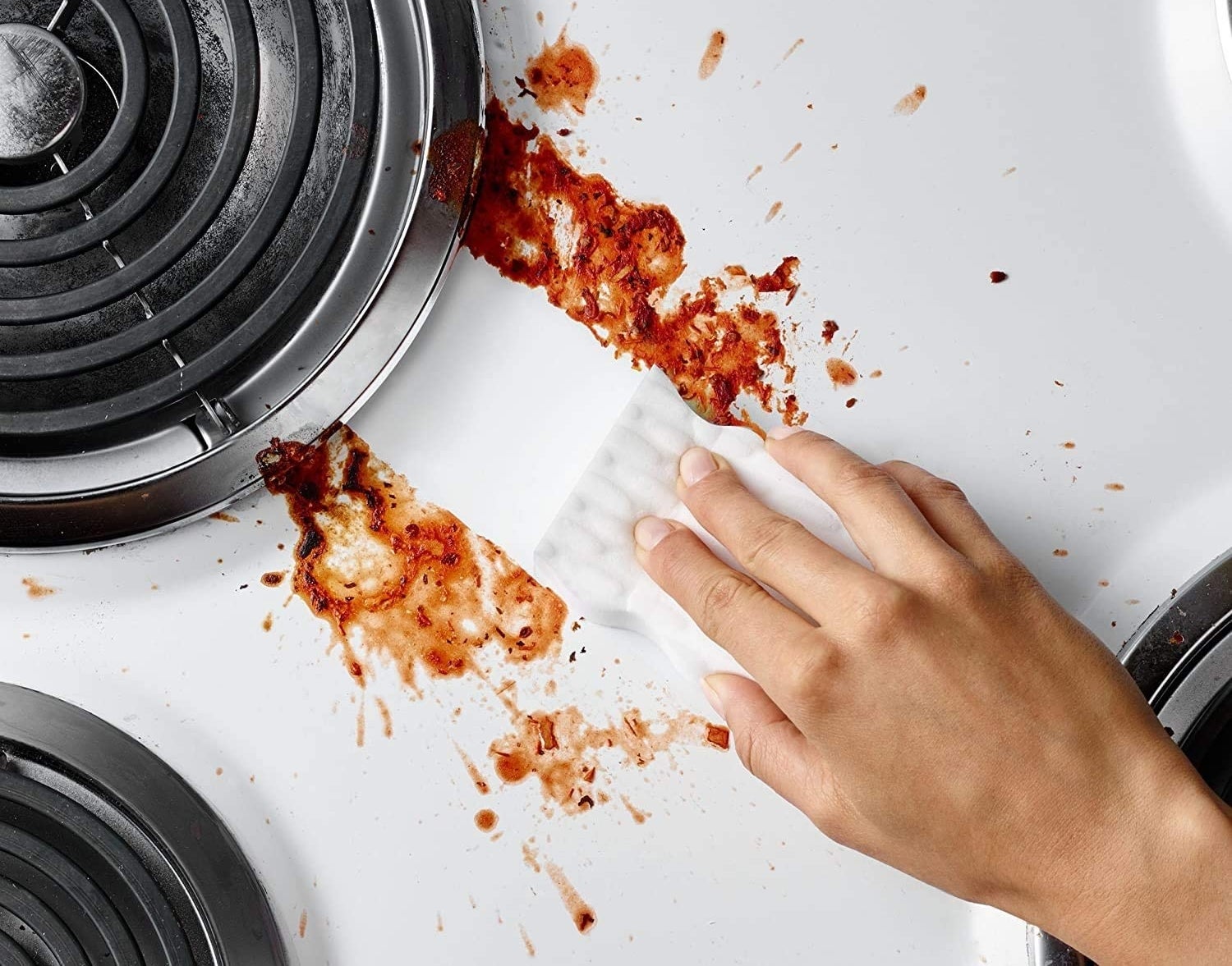 Magic eraser cloth swiping tomato sauce-splatted stove top clean