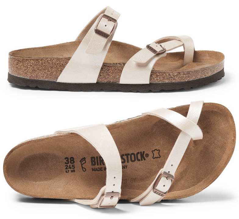 A three-strap, two-buckle white Birkenstock shoe with brown footbed; one strap goes across the top of your foot near your ankle; another goes across just below your toes, and a third goes across only your big toe. 