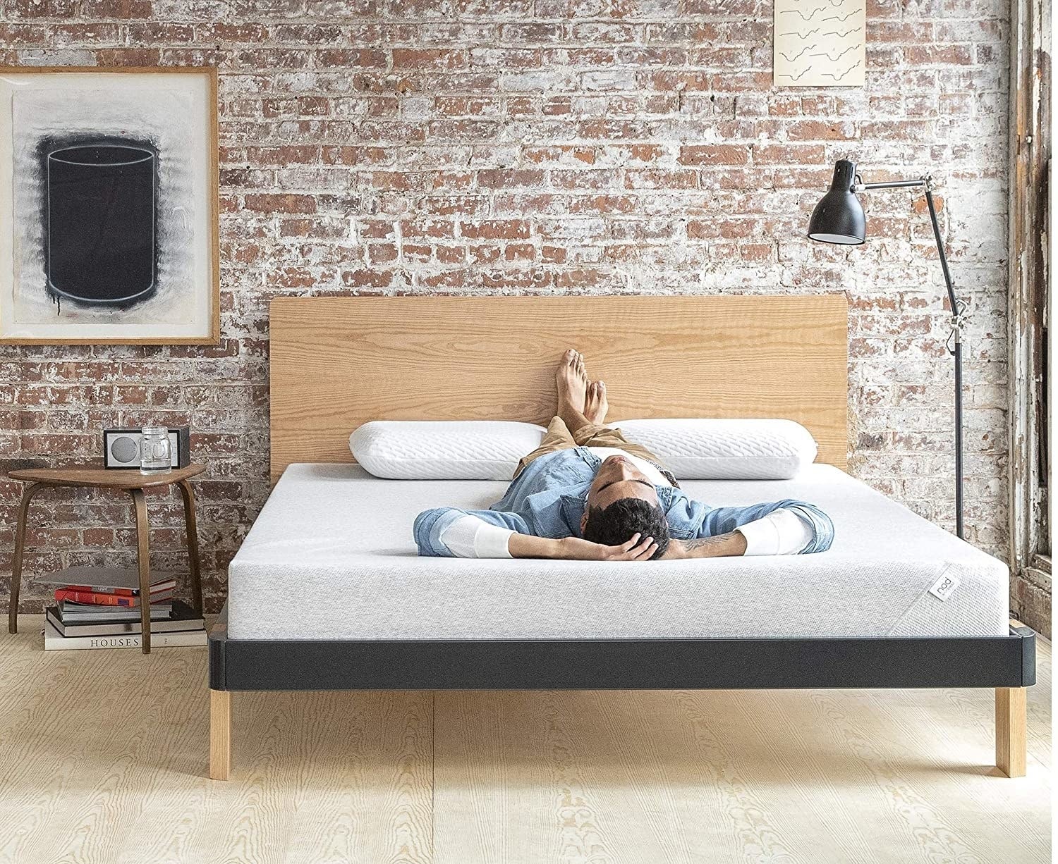 A person laying on their back with their hands behind their head on a gray mattress