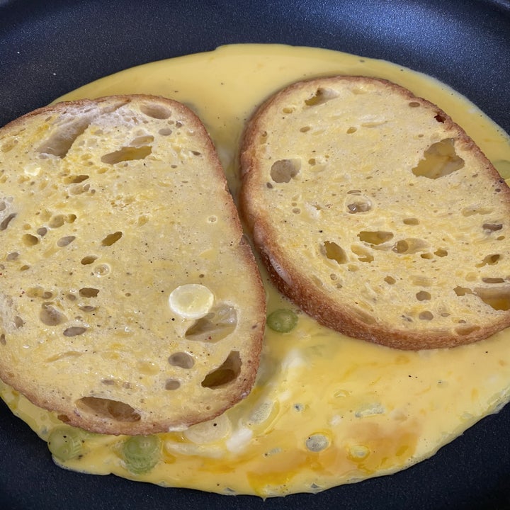 Two slices of bread in a skillet with uncooked scrambled eggs.