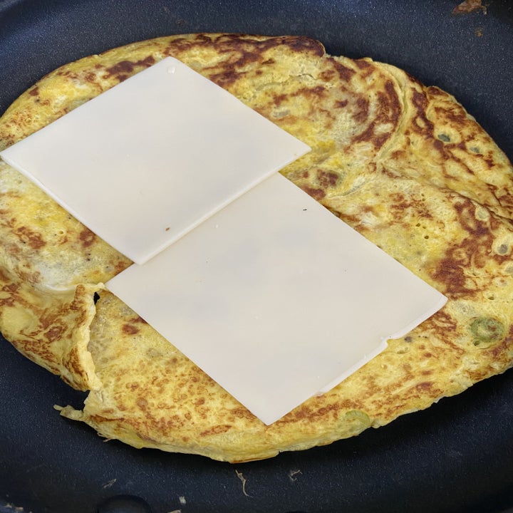 The omelet in a skillet with two slices of cheese on top.