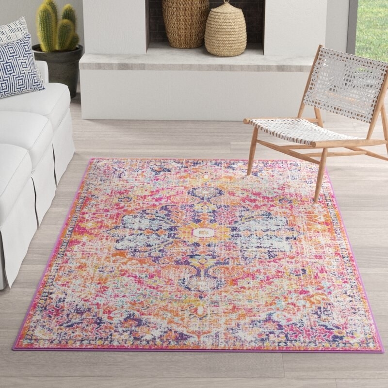 A large rug on the floor of a living room with a Persian-inspired, distressed pattern in bright colors