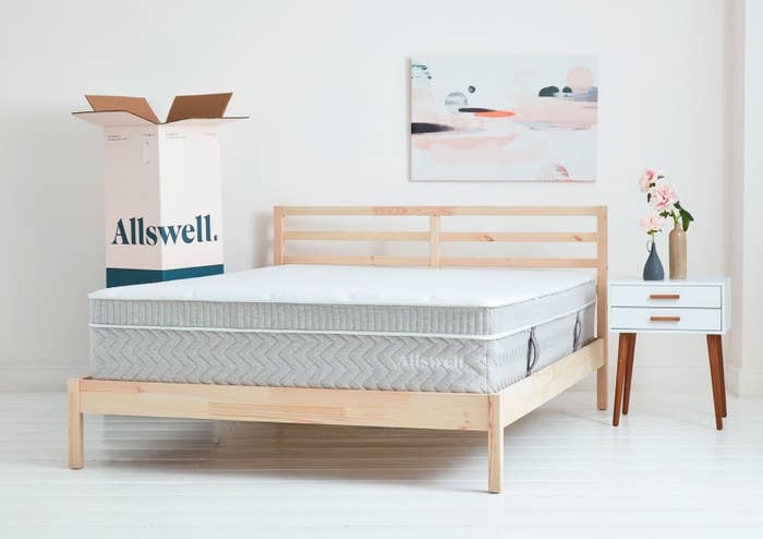 A bed-in-box mattress with a plush top in gray on a wooden bed frame next to the box it came in