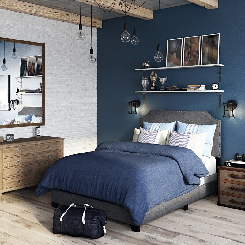 A gray upholstered bed staged in a fully made bedroom