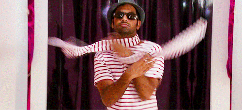 aziz ansari in the show "parks and recreation" throwing a striped scarf around his enck and saying "treat yo self"