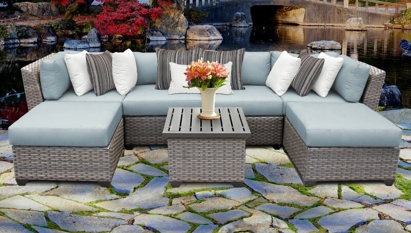 A large cushioned wicker outdoor seating couch in seven pieces that can be arranged in different ways, including a square table in the middle of them 