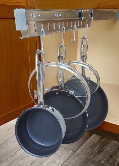 An organizer attached to the top of the inside of a cabinet, pulled out with pots, pans, and lids hanging from its hooks