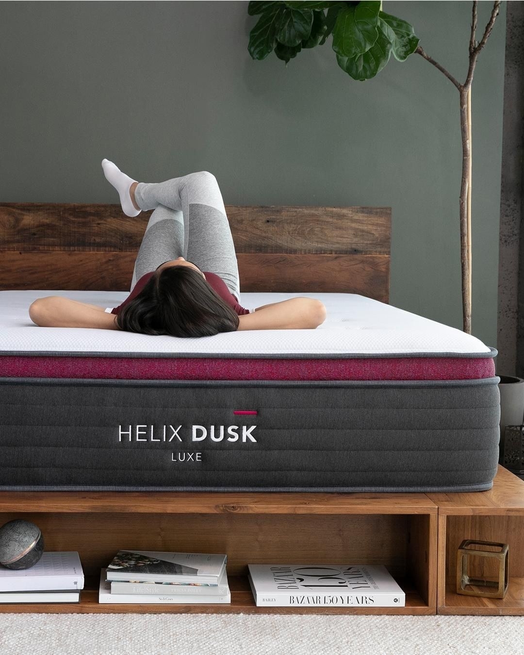 A person laying on their back with their hands behind their head on a gray mattress with a plush white top