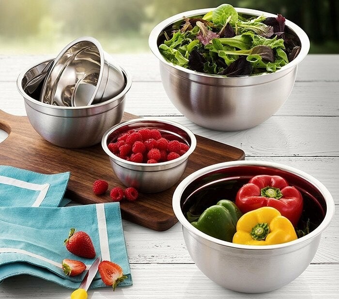 A set of five stainless steel mixing bowls of varying sizes holding produce