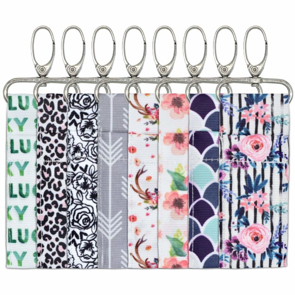 A flat lay of the clips in eight prints, from florals to pink leopard print. Each one is a small strip of fabric with a pocket to hold a lip balm and a large metal clip on the end.