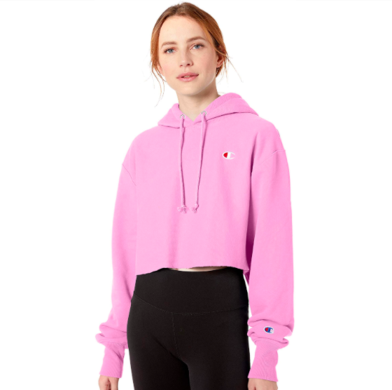 A model wearing the cropped hooded sweatshirt in bright pink with a small Champion logo on the chest