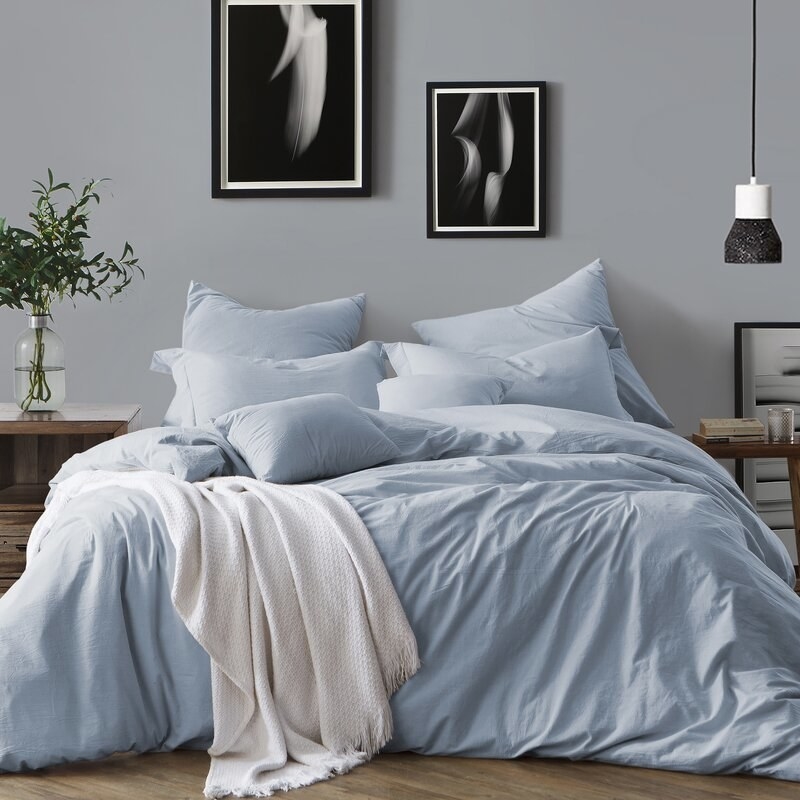 A bed with a very fluffy, long duvet with a blue duvet cover on it, displayed with match blue pillowcases