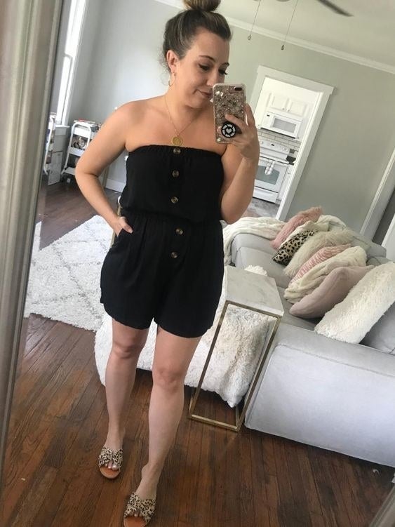 A reviewer wearing the strapless romper in black that's cinched in the middle and has brown buttons