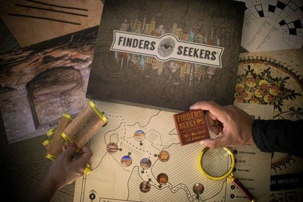 The Finders Seekers box cover, a map and magnifying glass, and two hands holding deciphering tools 