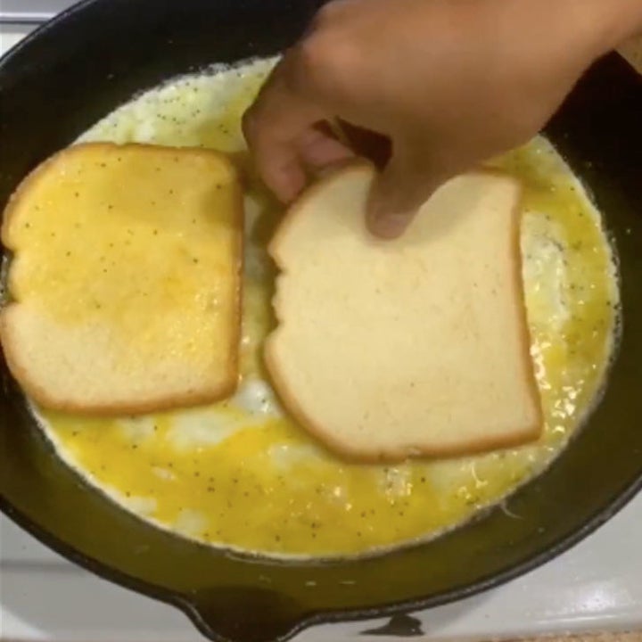 White bread being dipped into scrambled eggs in a skillet.