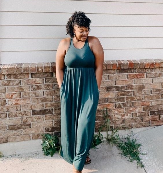 A reviewer wearing the sleeveless, cotton maxi dress that&#x27;s cinched below the chest in dark green