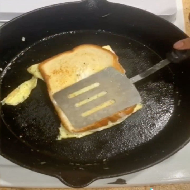 A breakfast sandwich filled with eggs in a skillet.