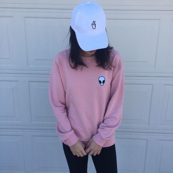 A reviewer wearing the pullover in light pink with the small white alien patch logo on the chest