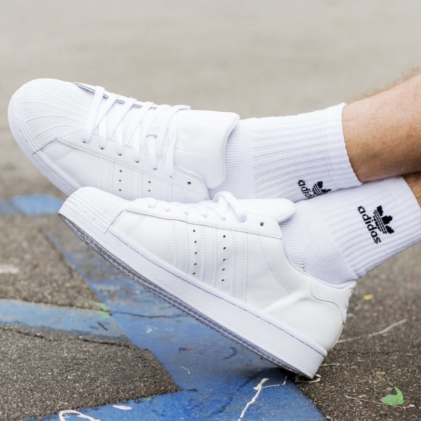 A pair of white Adidas Superstar sneakers worn by a model