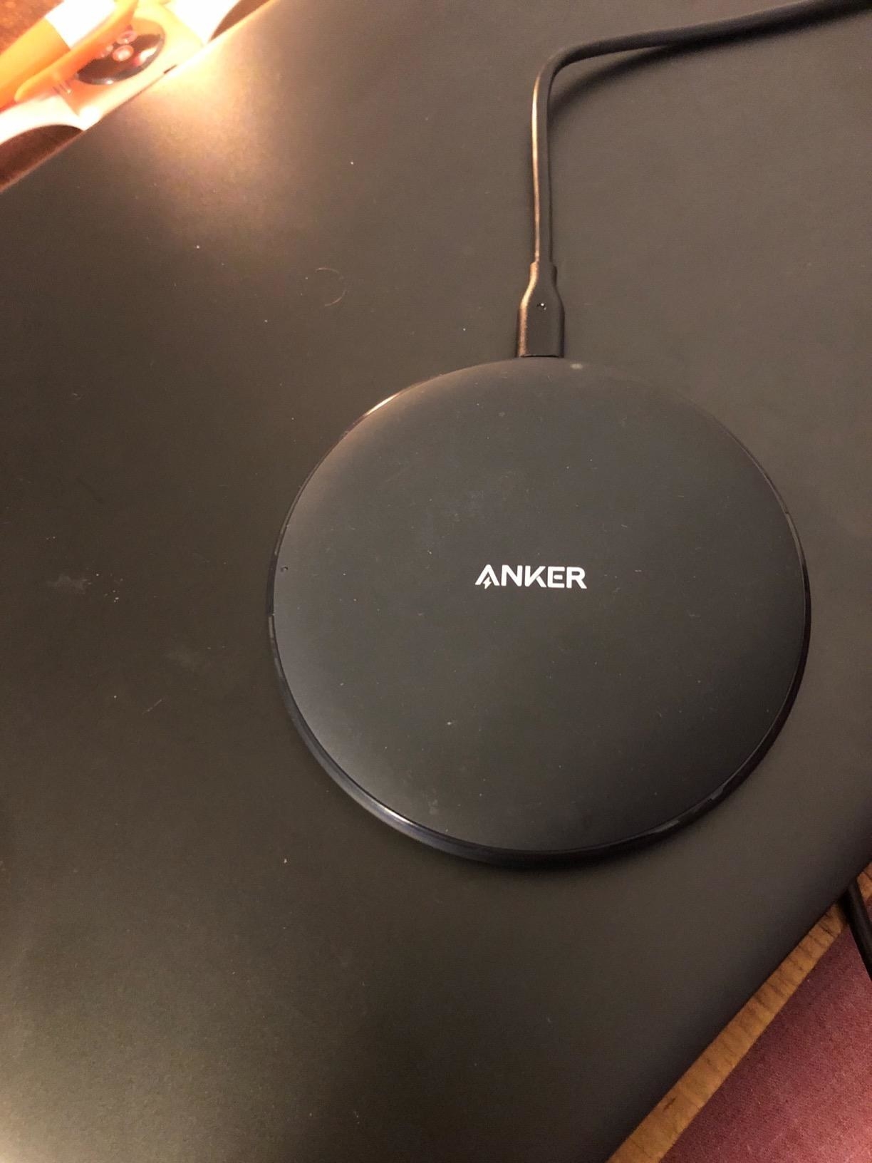 A round black Anker wireless charger sitting on a black tabletop