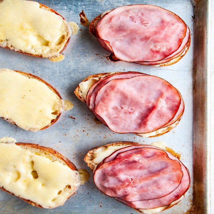 Slices of bread covered with cheese and sliced turkey on a sheet pan.