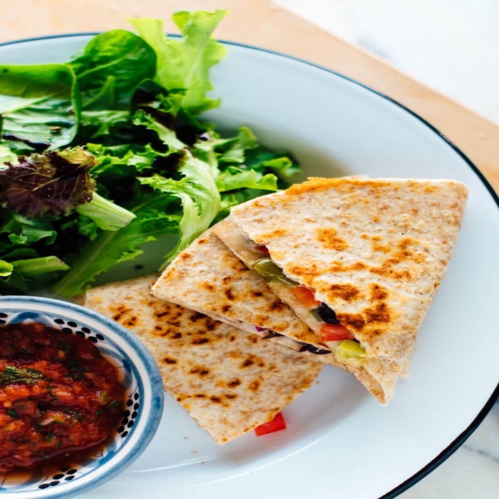 Sliced quesadillas stuffed with black beans, peppers, and corn on a plate with lettuce and salsa.