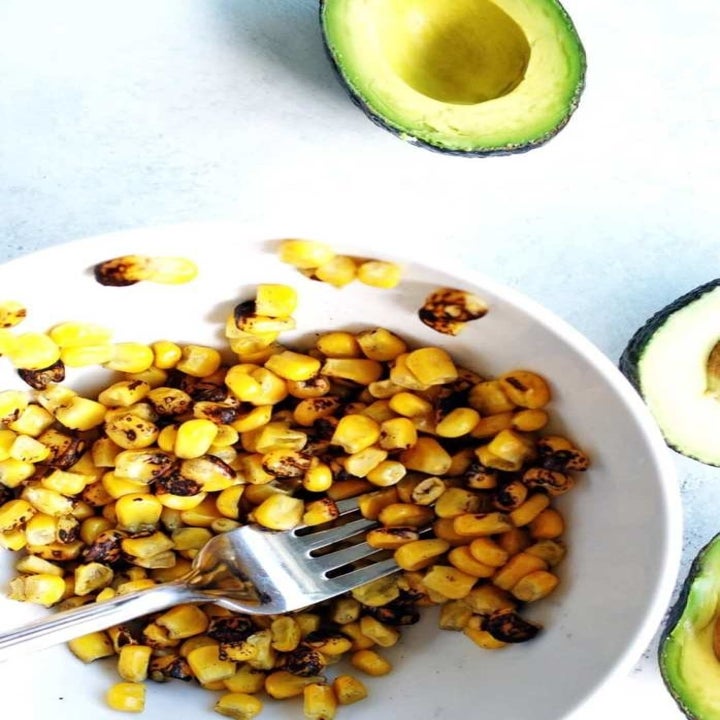 Corn kernels in a bowl with a half of an avocado on the side.