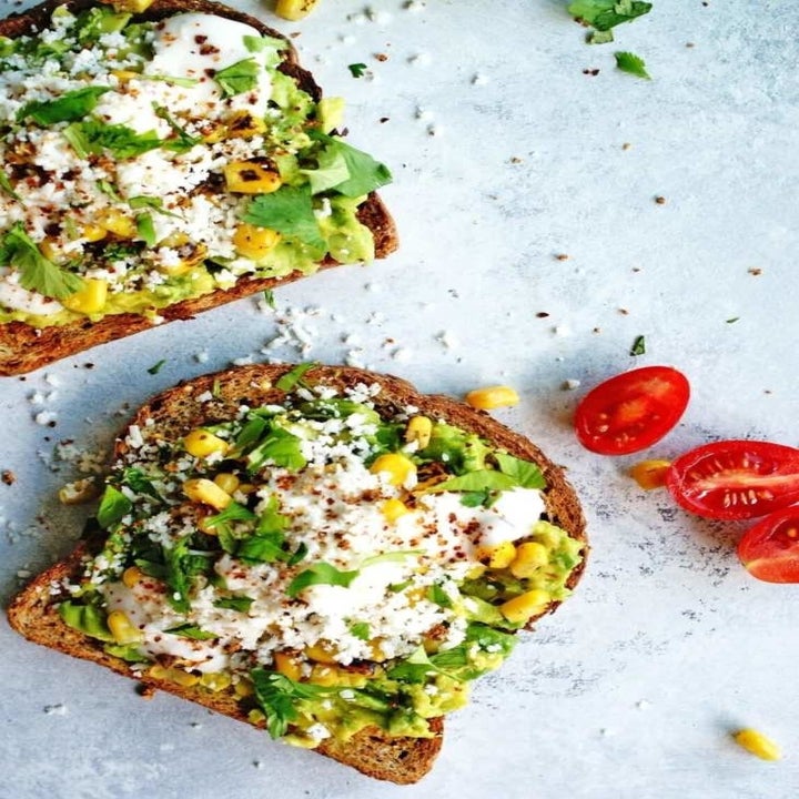 Two slices of whole wheat toast topped with smashed avocado, corn, and Cotijia cheese.
