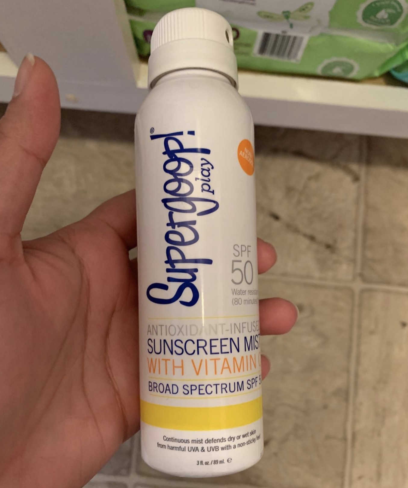 A reviewer&#x27;s hand holding the sunscreen spray bottle