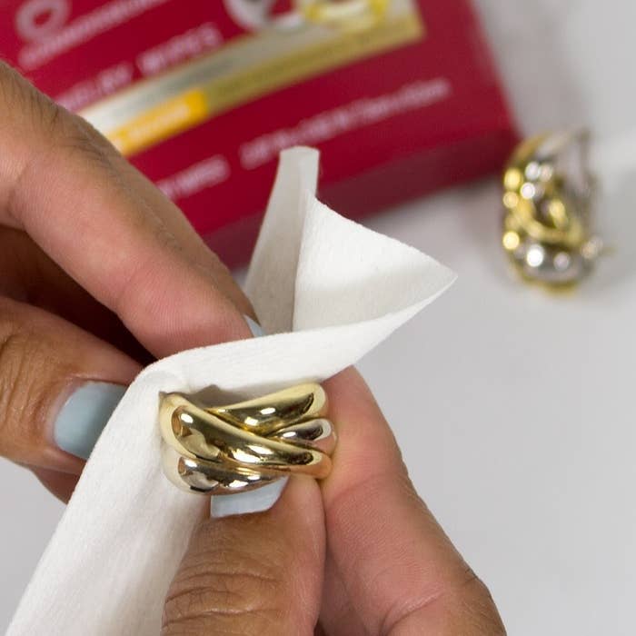 A person polishing a gold ring with a jewelry-cleaning wipe