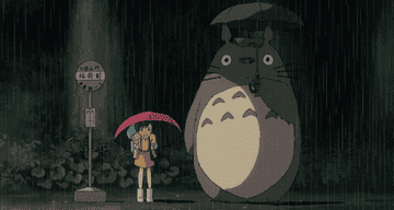 A GIF image of Totoro standing at a bus stop in the pouring rain holding an umbrella 