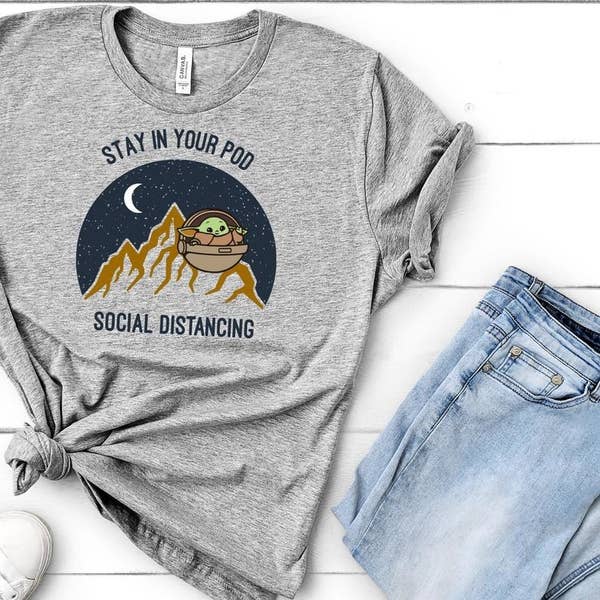 A shirt with a cartoon Baby Yoda that says "Stay in your pod" and "social distancing" 