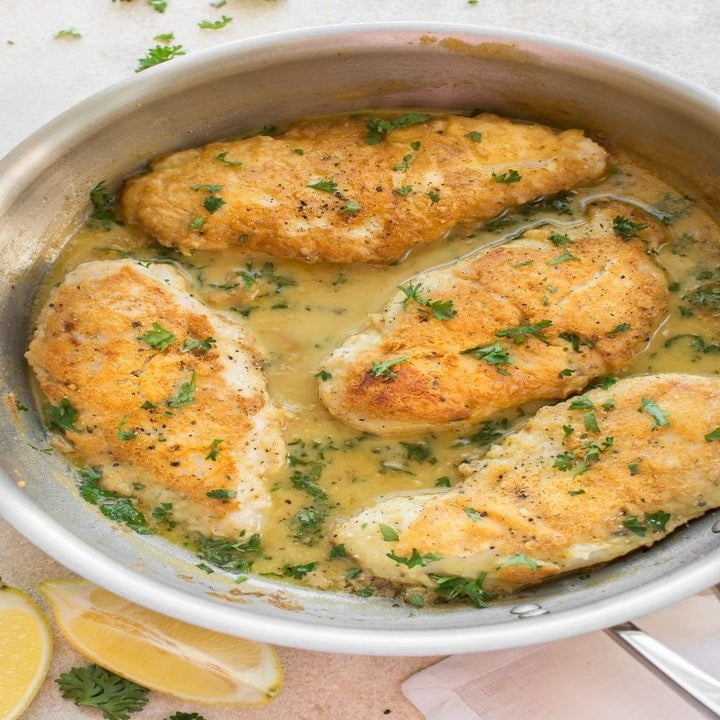A pan with four breaded chicken cutlets in a lemon and parsley sauce.