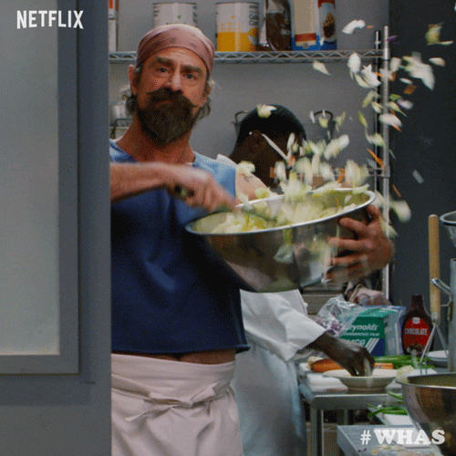 Christopher Meloni in the series "wet hot american summer: first day of camp" tossing a salad in a large bowl, spilling it everywhere