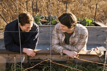 Sam and Grizz from &quot;The Society&quot; laugh, sitting close together while hunched over a flowerbed