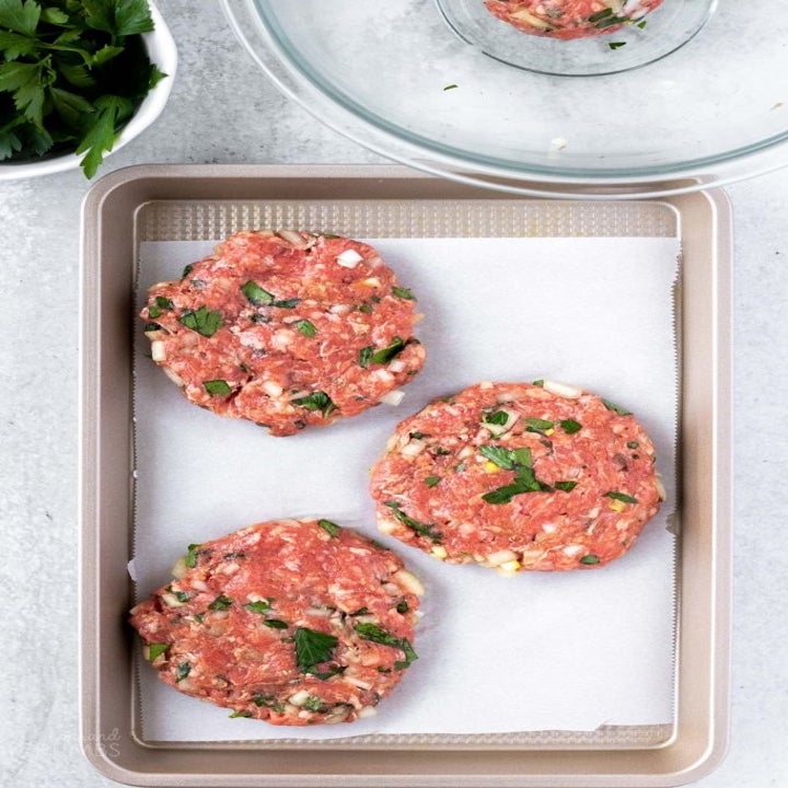 Three uncooked hamburger patties on a sheet pan.