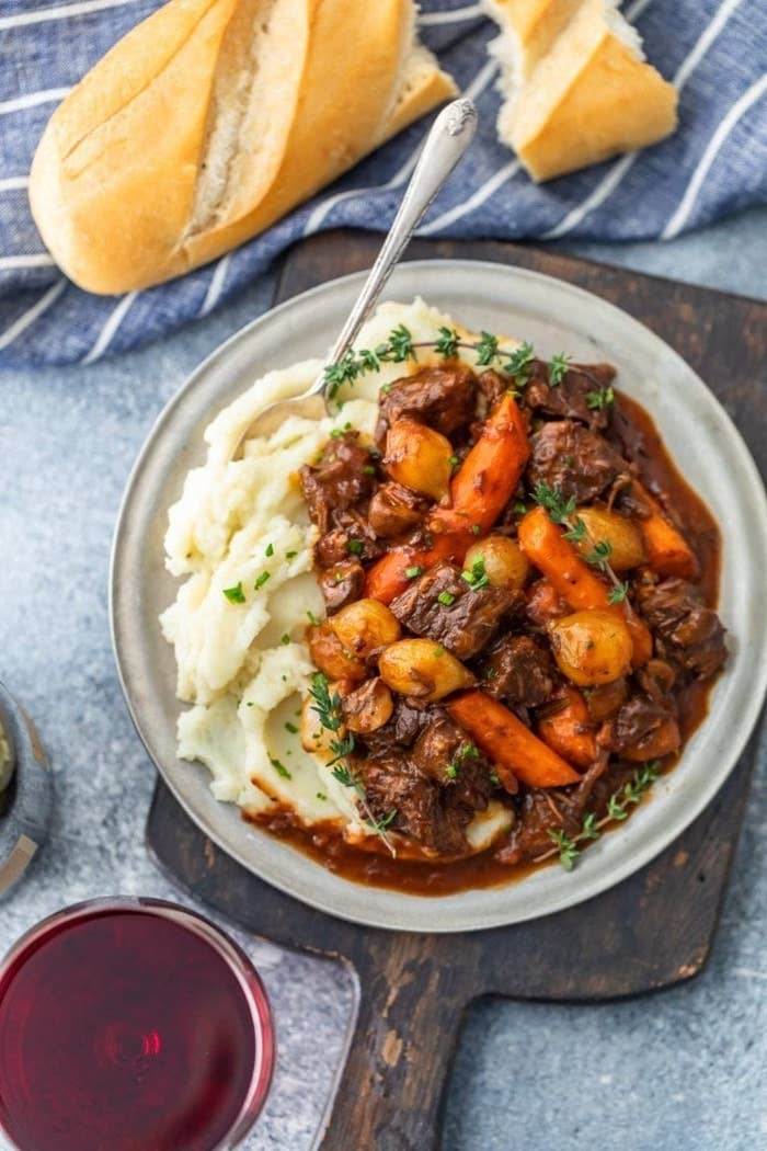 A big bowl of beef stew with carrots on top of creamy mashed potatoes.