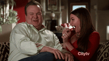 gif from modern family of two people laughing and shimmying on couch