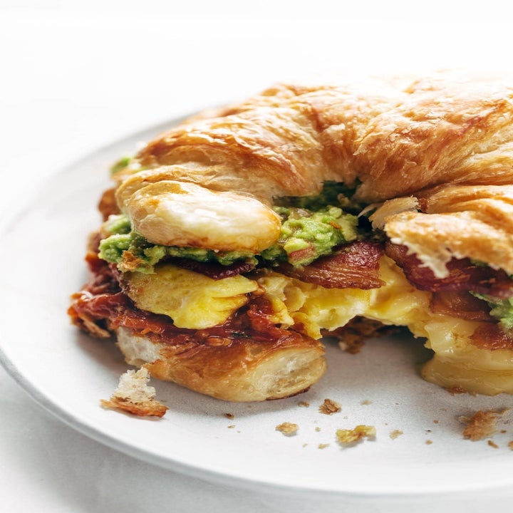 A breakfast sandwich with bacon, avocado, and soft scrambled eggs on a croissant.