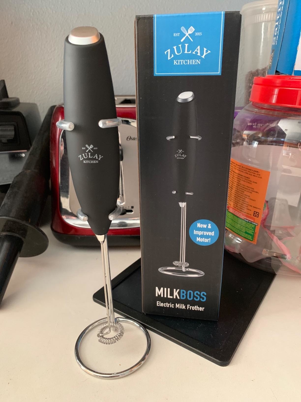 A dark-gray milk frother stood next to its packaging