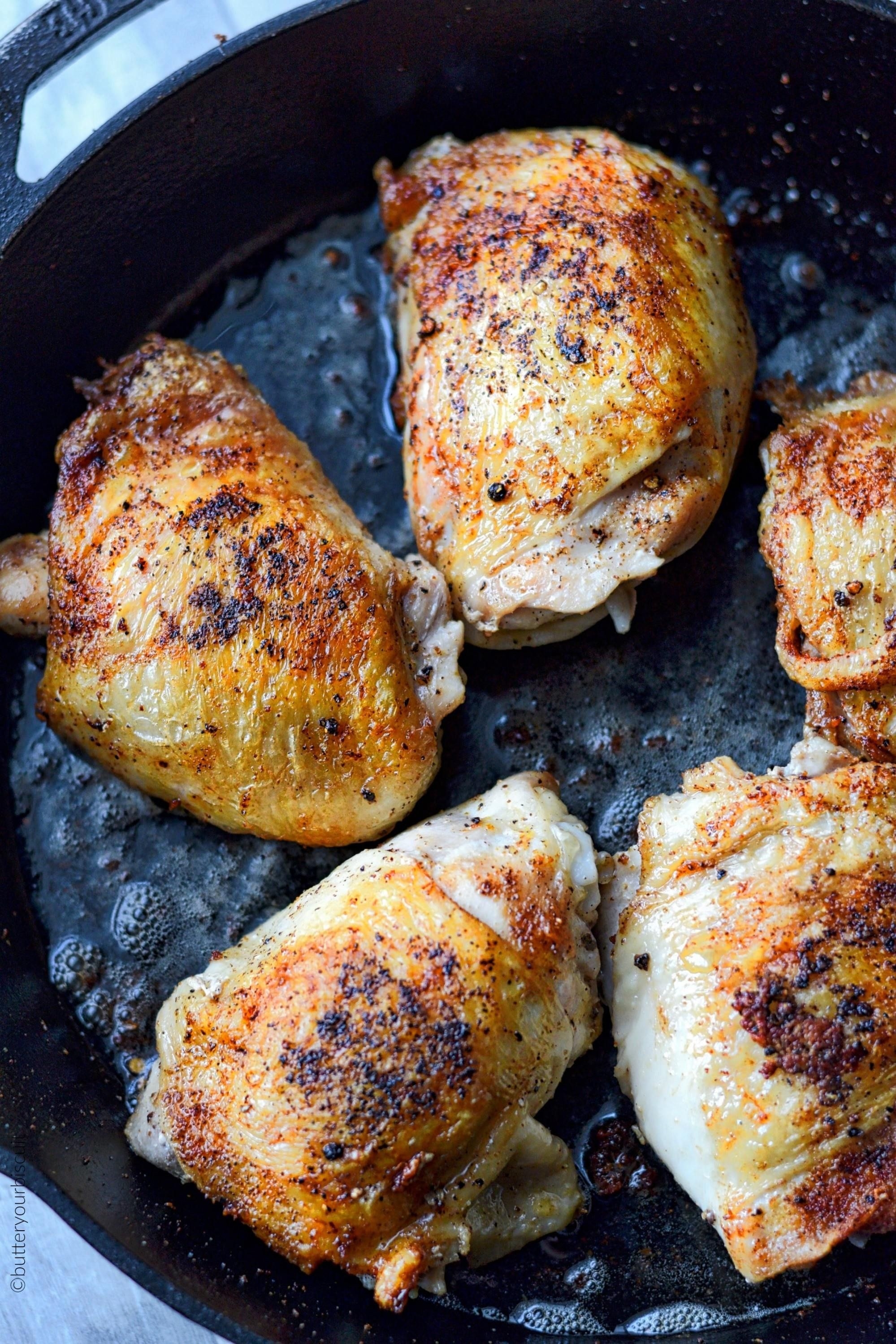 A cast iron skillet with five pieces of crispy chicken thighs in sizzling oil.