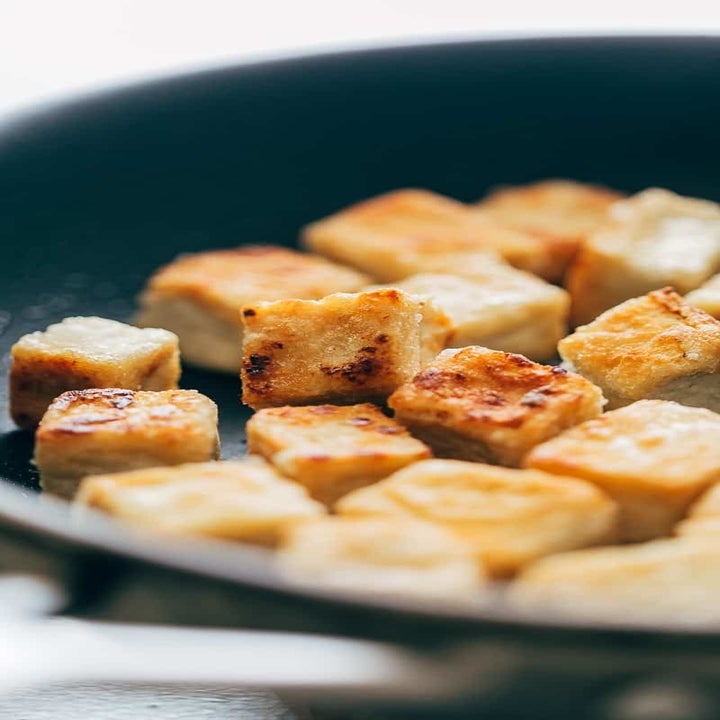 Cubes of tofu cooking in a skillet.